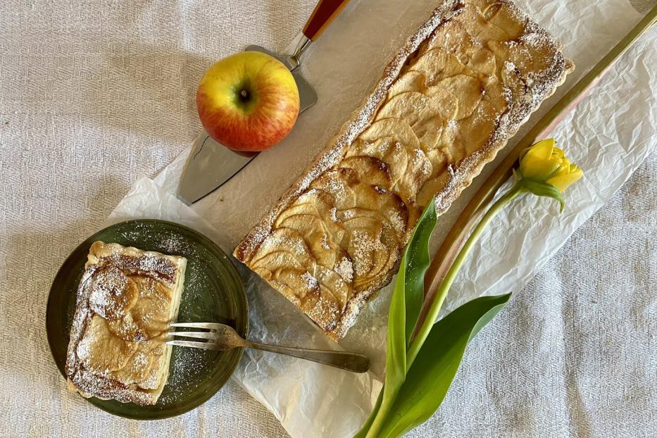 Ein Apfel-Rhabarber-Kuchen neben einer gelben Blume und einem Apfel.