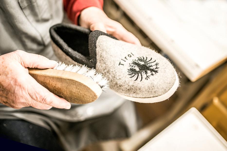 Eine Person bürstet einen grauen Filzpantoffel mit Tiroler Adler-Emblem.