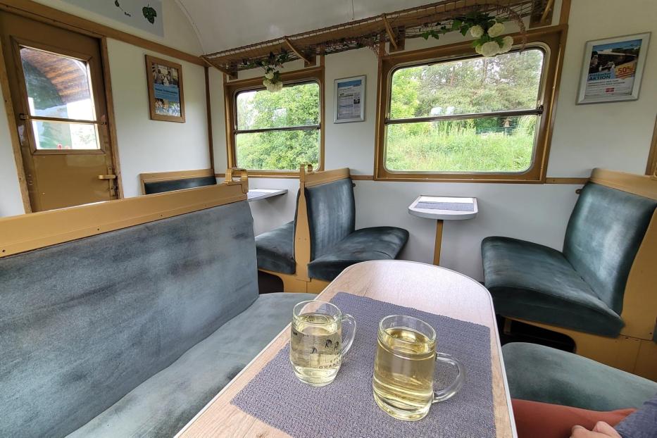 Ein Speisewagen in eine Zug; vorne im Bild ist ein Tisch mit zwei Gläsern Weißwein zu sehen.