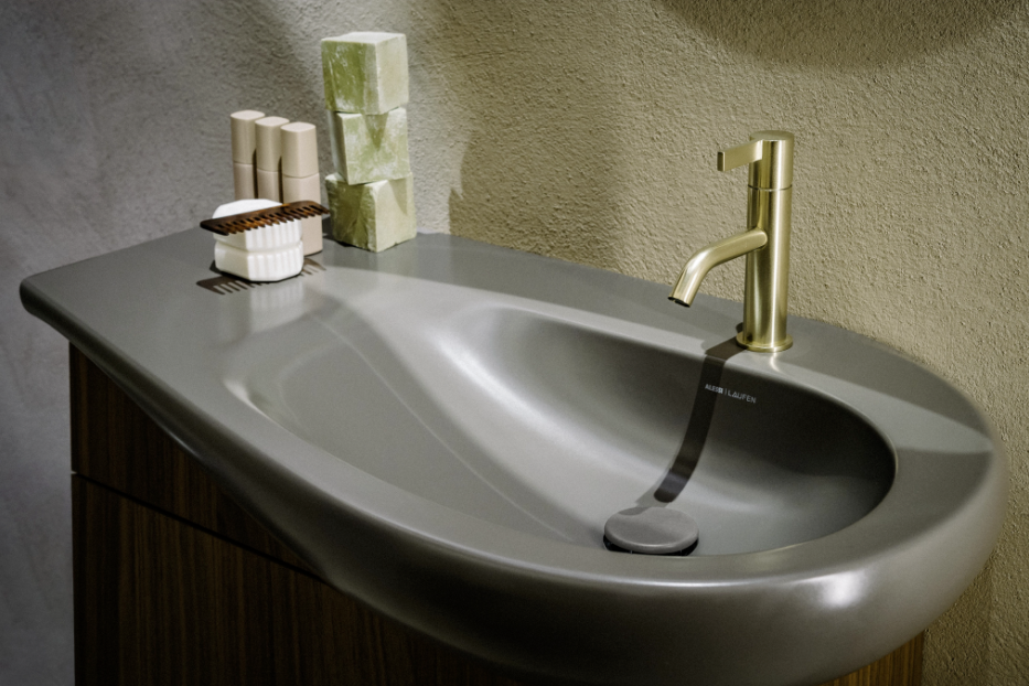 Ein schwarzes Waschbecken von LAUFEN mit einem goldenen LAUFEN-Wasserhahn. 
