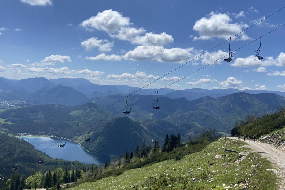 Bergausblick auf einen im Tal liegenden See mit grüner Hügellandschaft im Hintergrund.