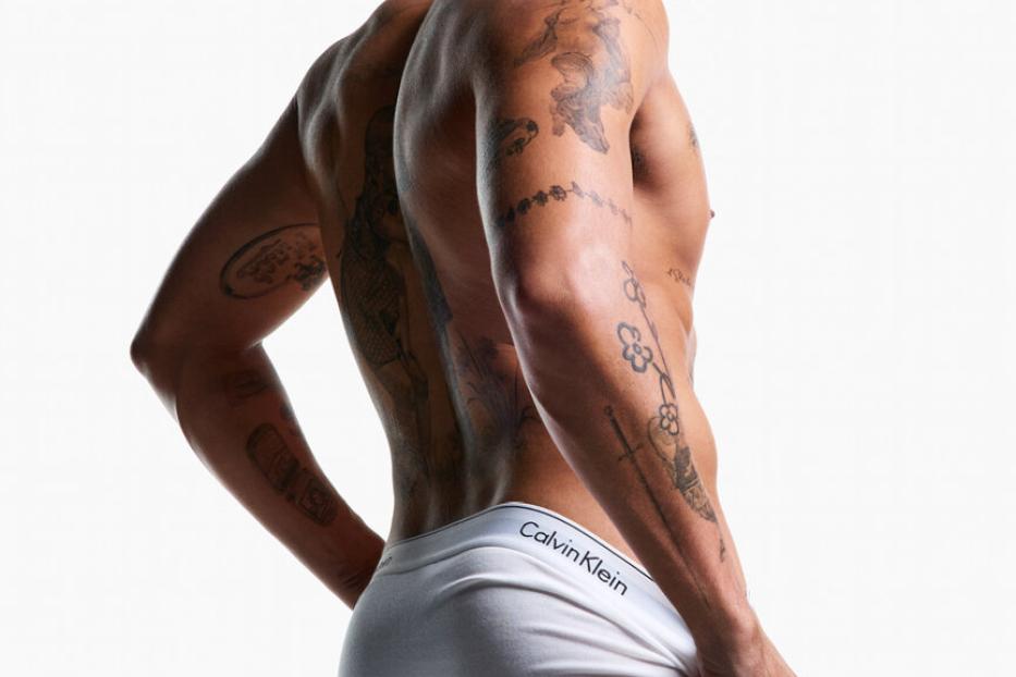 Ein Mann mit Tätowierungen trägt weiße Calvin Klein Unterwäsche.