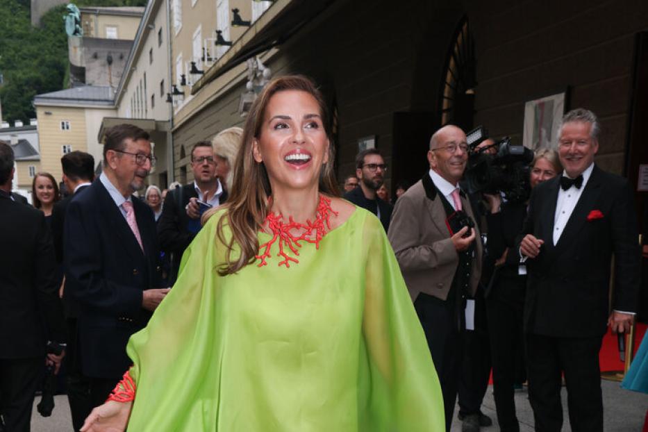 Eine Frau in einem hellgrünen Kleid und einer roten Korallenkette lächelt in die Kamera.