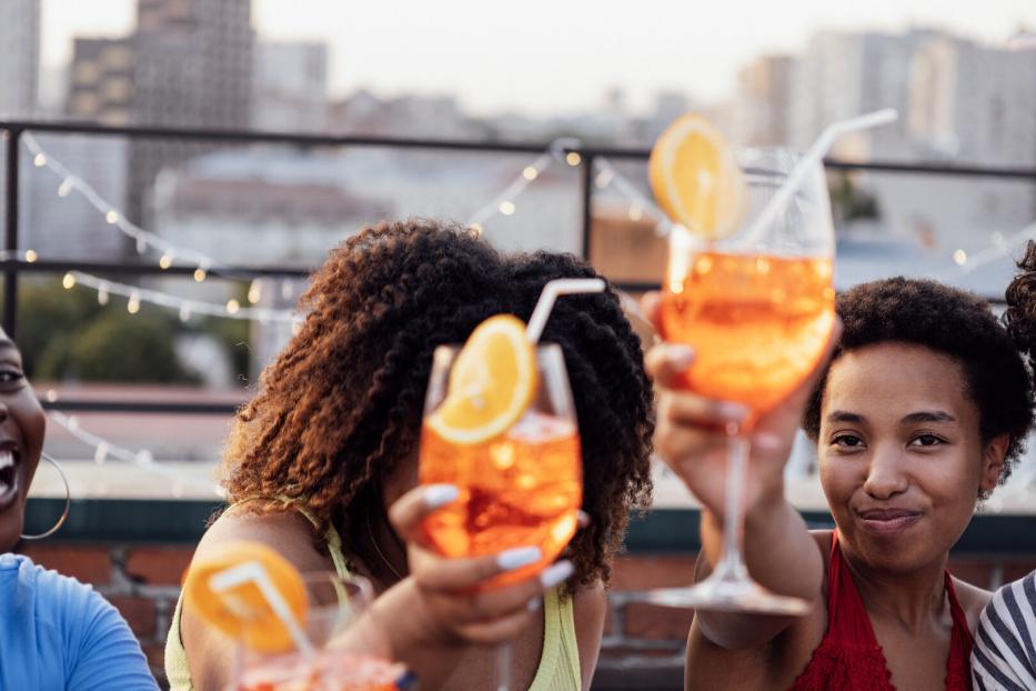 Freunde - offenbar in einer Rooftop-Bar in New Yorkt - prosten einander mit Aperol Spritz zu