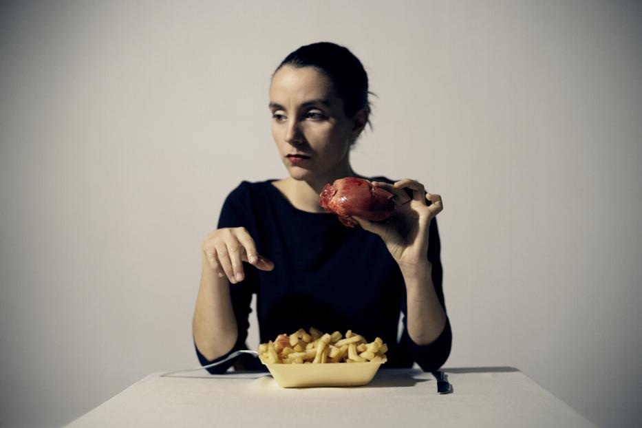 Die Künstlerin hinter einer großen Schale Pommes Frites - dazu hält sie ein (wohl künstliches) Herz in der Hand.