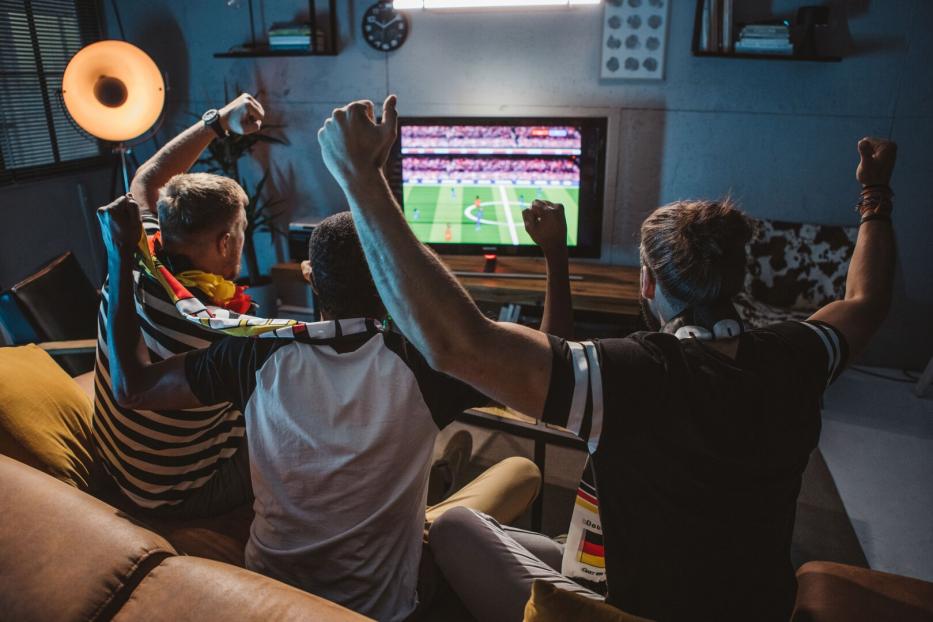 Fußballfans sitzen gemeinsam vor dem Fernseher und jubeln.