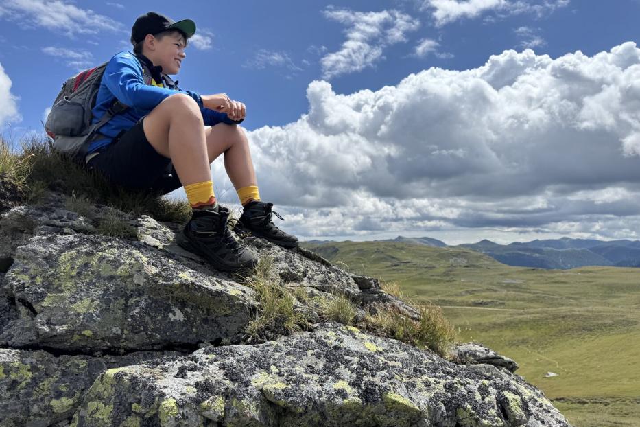 Kind sitzt auf einem Felsen und schaut in die Landschaft