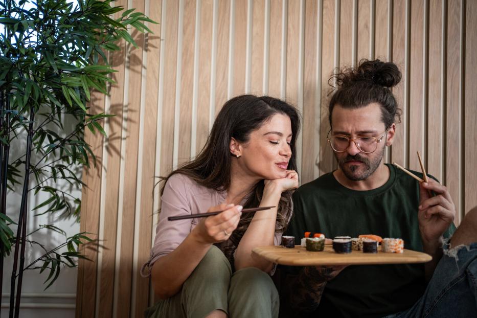 Ein junges Paar isst Sushi, die Frau möchte vom Teller des Mannes naschen.