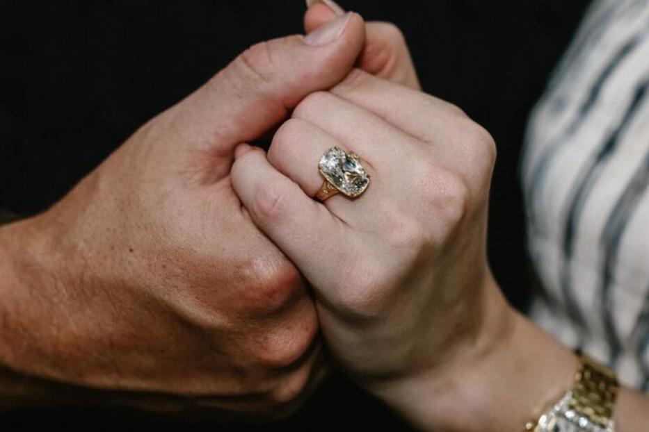 Ein Paar hält Händchen, wobei ein großer Diamantring an der Hand der Frau zu sehen ist.