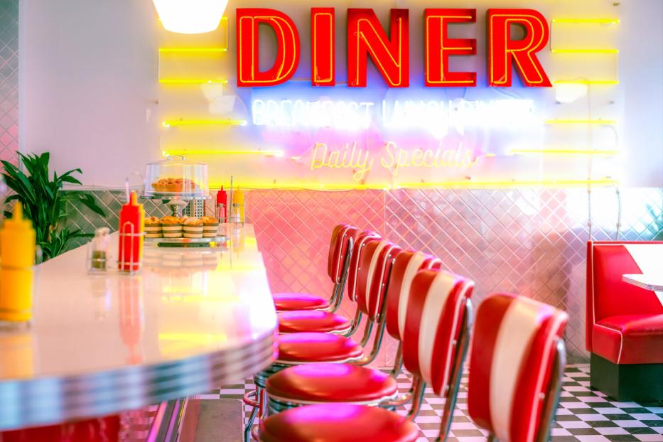 Das Interieur eines leeren Diners mit roten Barhockern und Neonreklame.