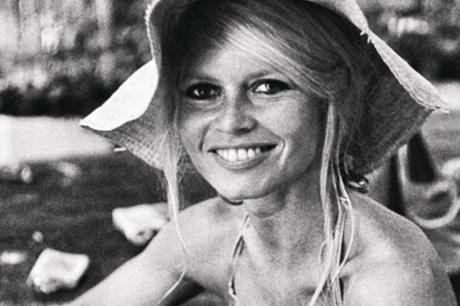 Brigitte Bardot mit Hut und Gitarre lächelt.