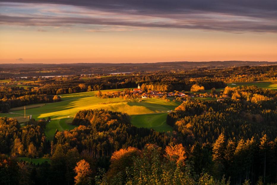 Landschaft mit Feldern, Wald und Dorf bei Sonnenuntergang mit orangefarbenem Himmel.