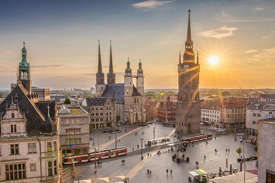 Sonnenuntergang über einem Stadtplatz mit markanten Türmen im Hintergrund.