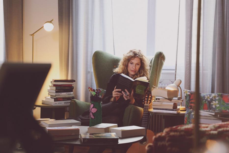 Lotte de Beer beim Lesen in einem Sessel - vor ihr türmen sich Bücher.