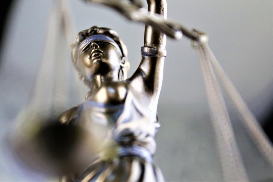 Eine silberne Justitia-Figur mit verbundenen Augen hält eine Waage in der erhobenen Hand.