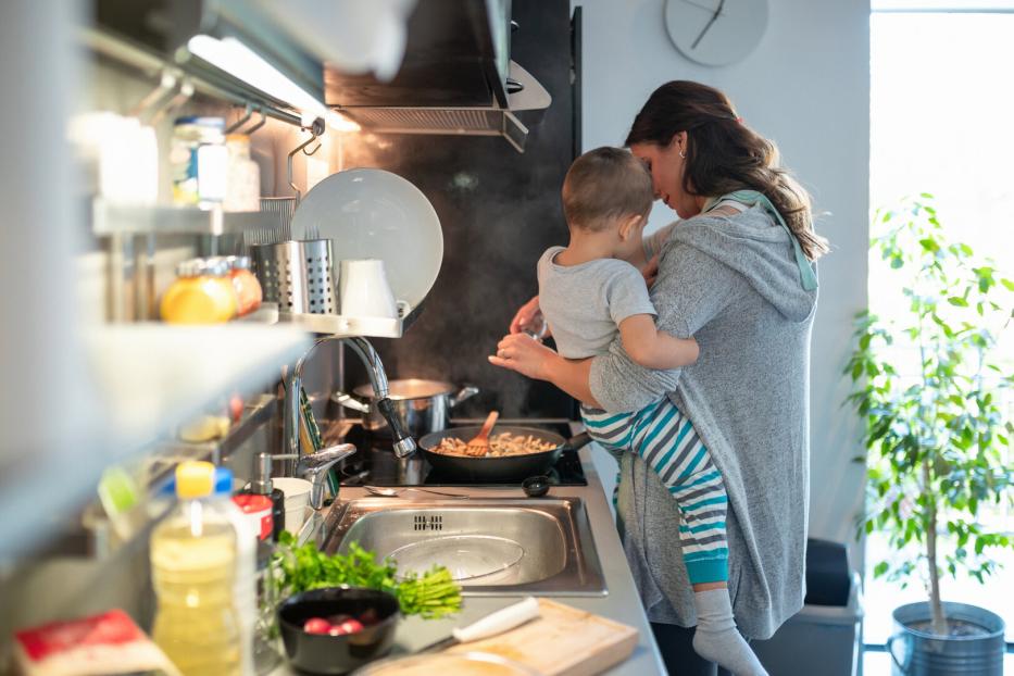 Mother carrying toddler on hip and preparing meal