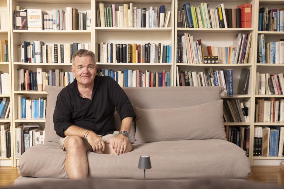 Cornelius Obonya sitzt lässig auf einer Couch vor seinem Bücherregal.