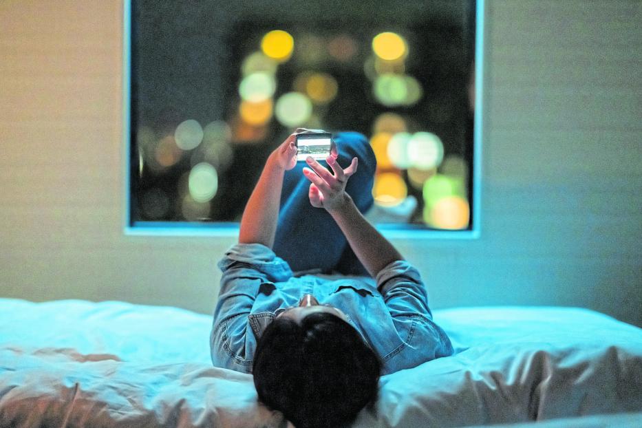 Woman lying down on bed and using smart phone at night