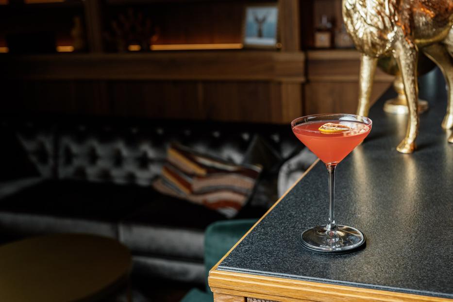 Romy Cocktail, in einer dunklen Bar auf einem Tisch ein Orangener Cocktail in einem edlen Glas