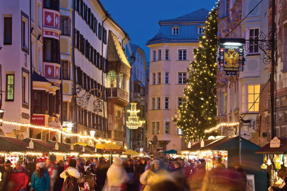 Ein belebter Weihnachtsmarkt in Innsbruck mit geschmücktem Baum und dem Gasthof Goldener Adler im Hintergrund.