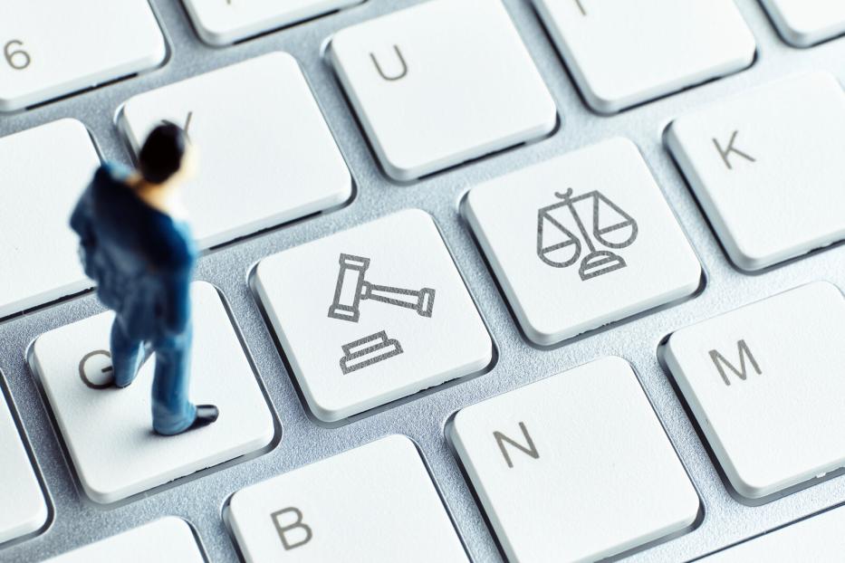 Eine kleine Figur steht auf einer Computertastatur mit Tasten, die Richterhammer und Waage zeigen.