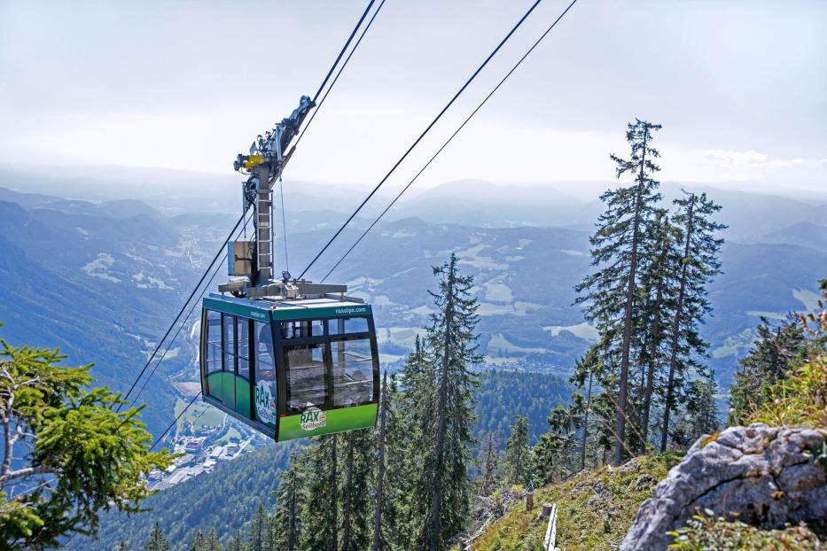 Eine grüne Rax-Seilbahn schwebt vor einer Berglandschaft.