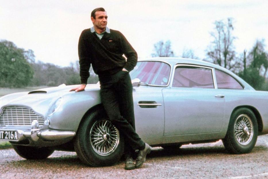 Sean Connery lehnt lässig an einem silbernen Aston Martin DB5 mit dem Kennzeichen BMT 216A.