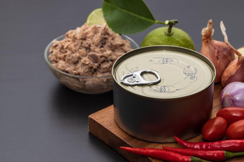 Eine ungeöffnete Konservendose steht neben einer Schale mit Thunfisch, Limette, Schalotten, Tomaten und roten Chilischoten.