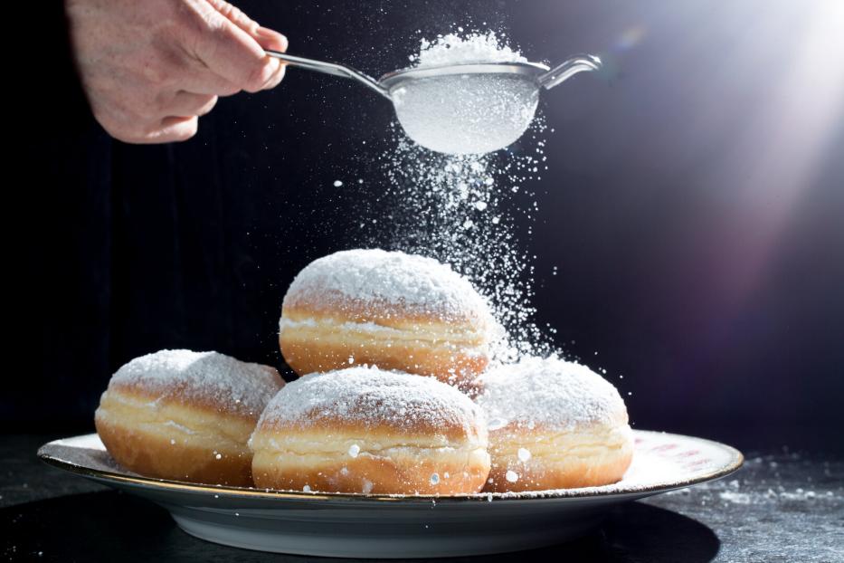 Ein Teller Krapfen wird mit Puderzucker bestreut.