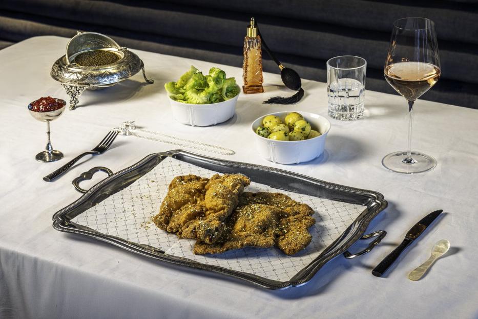 Auf einem gedeckten Tisch stehen Schnitzel auf einem Serviertablett, dazu Salat, Kartoffeln, Kaviar und Getränke.