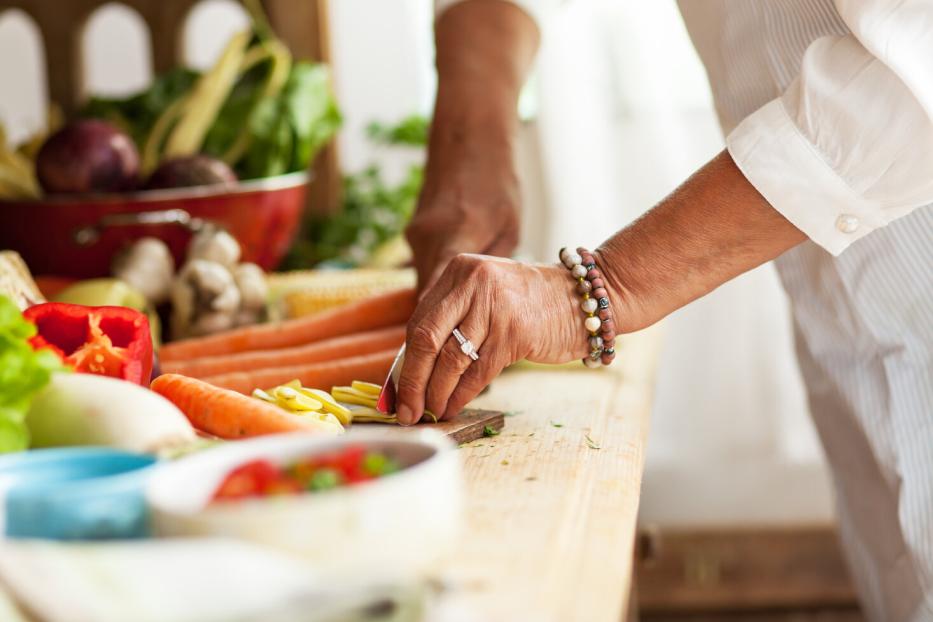 Eine Person schneidet frisches Gemüse auf einem Holztisch, umgeben von weiteren Gemüsesorten.