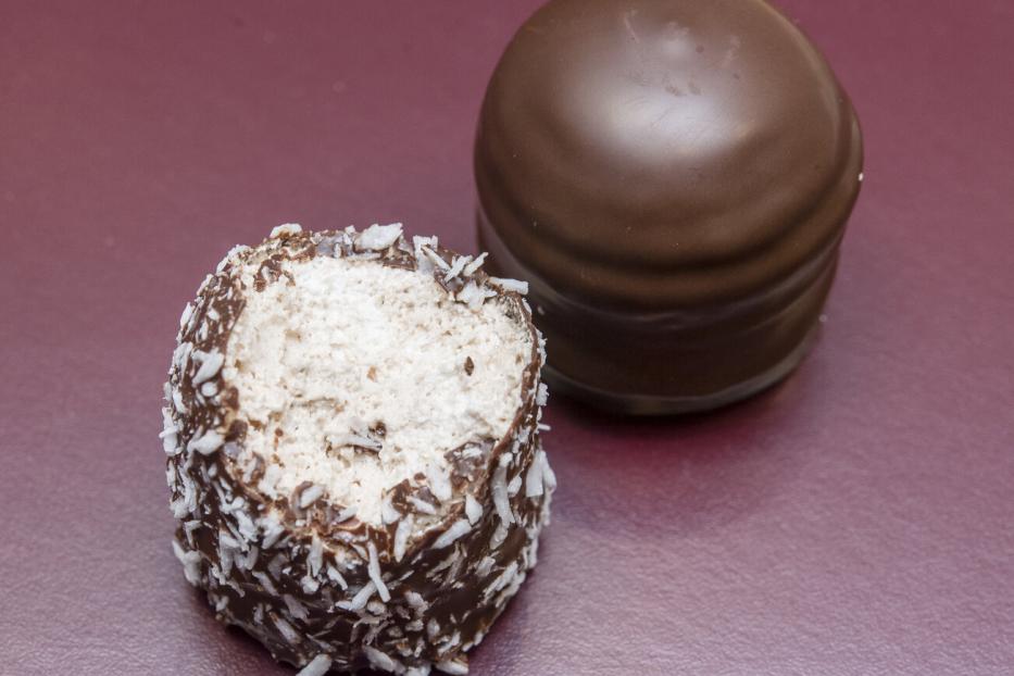 Zwei Schokoküsse, einer davon mit Kokosraspeln und angebissen, auf einer roten Oberfläche.