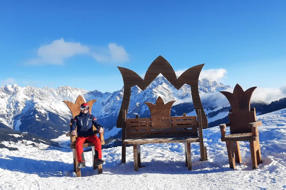 Ein Skifahrer sitzt auf einem Thron vor einer verschneiten Berglandschaft.