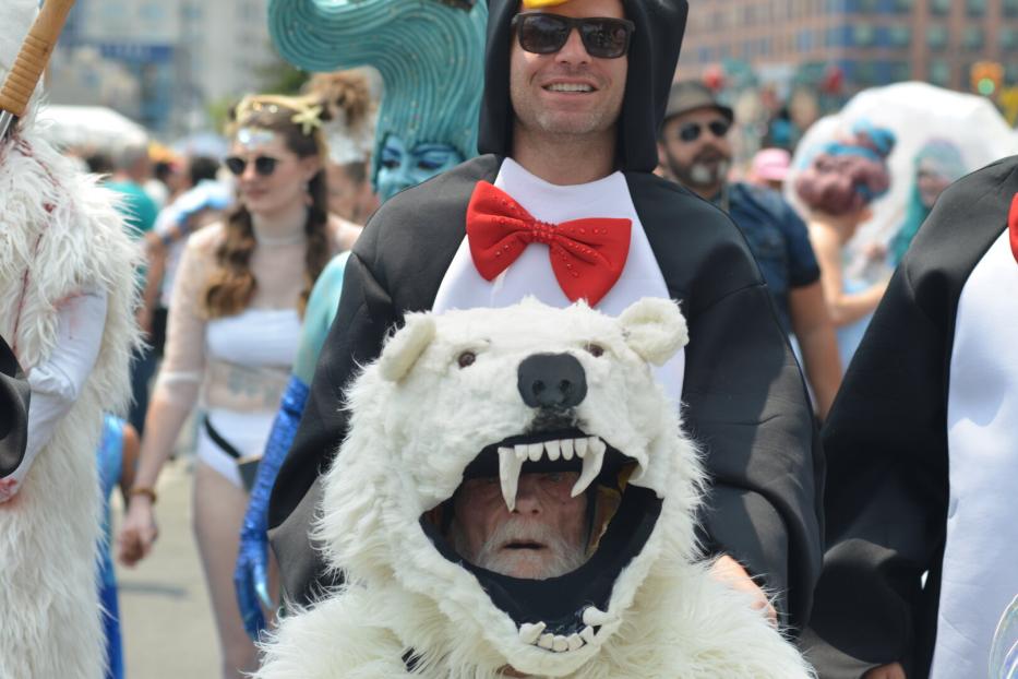 Mehrere Menschen in fantasievollen Kostümen, darunter ein Pinguin mit roter Fliege und ein Eisbärkostüm mit offenem Maul.