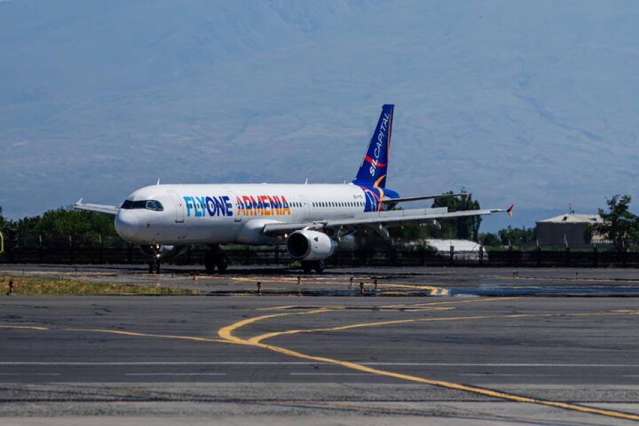 Ein Flugzeug von FlyOne Armenia steht vor einem schneebedeckten Berg auf einer Startbahn.