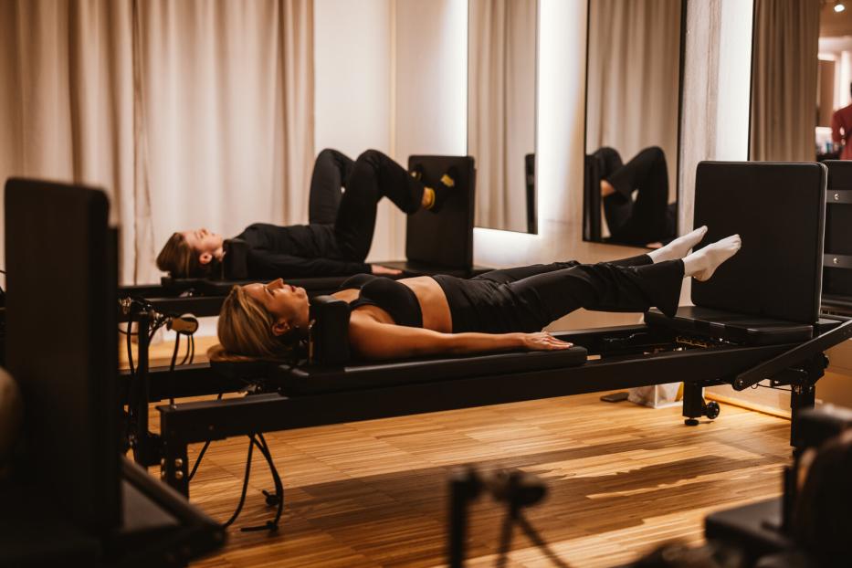 Zwei Frauen trainieren auf Pilates-Reformer-Jumpboard-Geräten in einem hellen Studio.