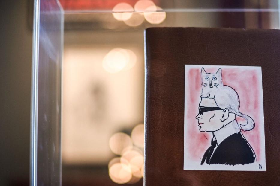 Ein Bild zeigt eine Zeichnung von Karl Lagerfeld mit seiner Katze Choupette auf dem Kopf.