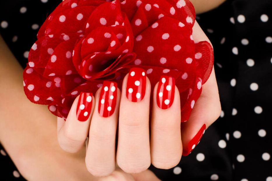 Rote Fingernägel mit weißen Punkten, dazu eine rote Stoffblume und schwarzer Stoff mit weißen Punkten.