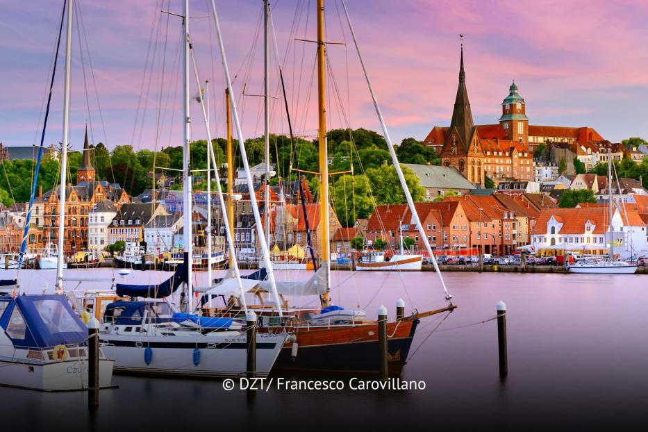 Segelboote im Hafen vor historischer Altstadtkulisse und Kirchen bei Sonnenuntergang in Flensburg.