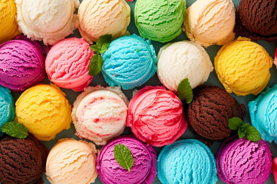 Viele bunte Eiskugeln in verschiedenen Geschmacksrichtungen, einige mit Minzblättern garniert, liegen dicht nebeneinander.