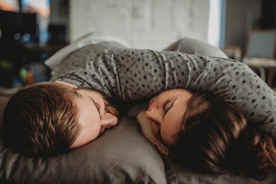 Zwei Menschen liegen eng umarmt auf einem Kissen und schlafen mit geschlossenen Augen nebeneinander.