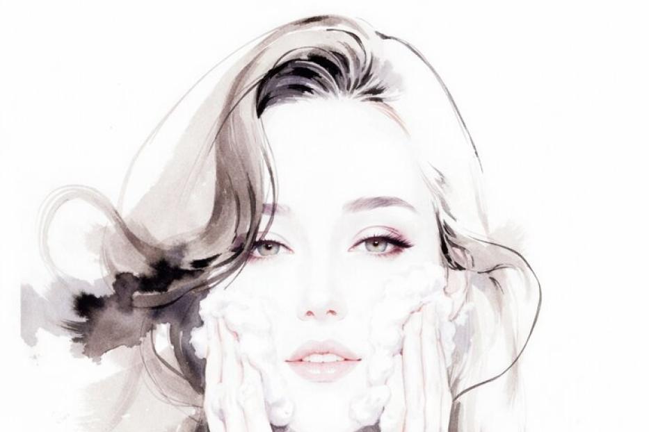 Eine Frau mit schulterlangem Haar wäscht ihr Gesicht mit Schaum und trägt ein schwarzes Oberteil.