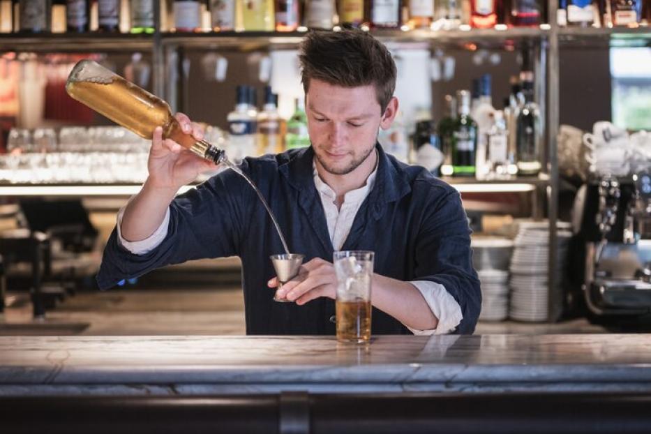 Ein Barkeeper gießt eine Flüssigkeit aus einer Flasche in einen Messbecher an einer Bar.