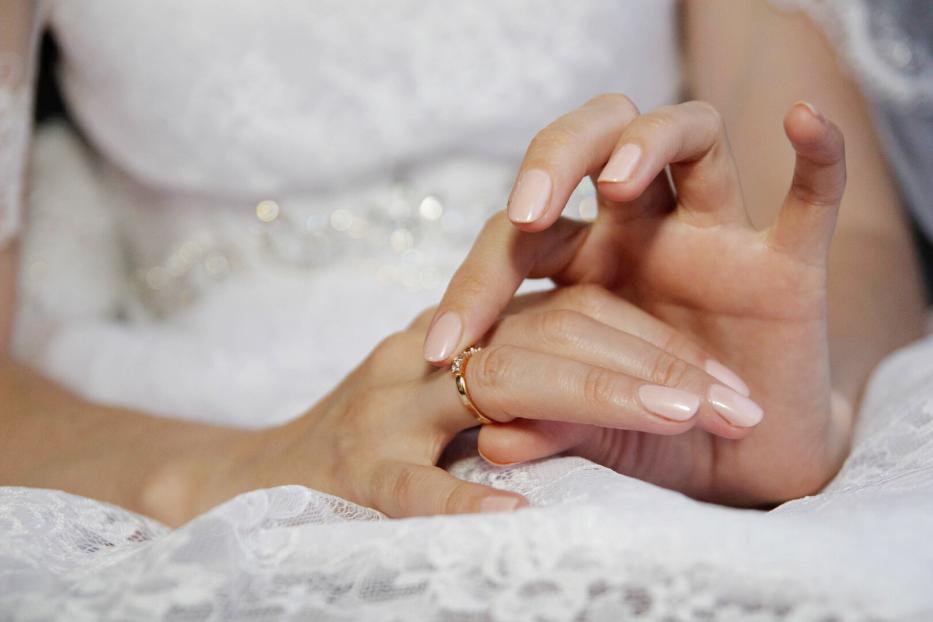 Eine Frau in weißer Spitze steckt sich einen goldenen Ring mit Stein an den Finger.