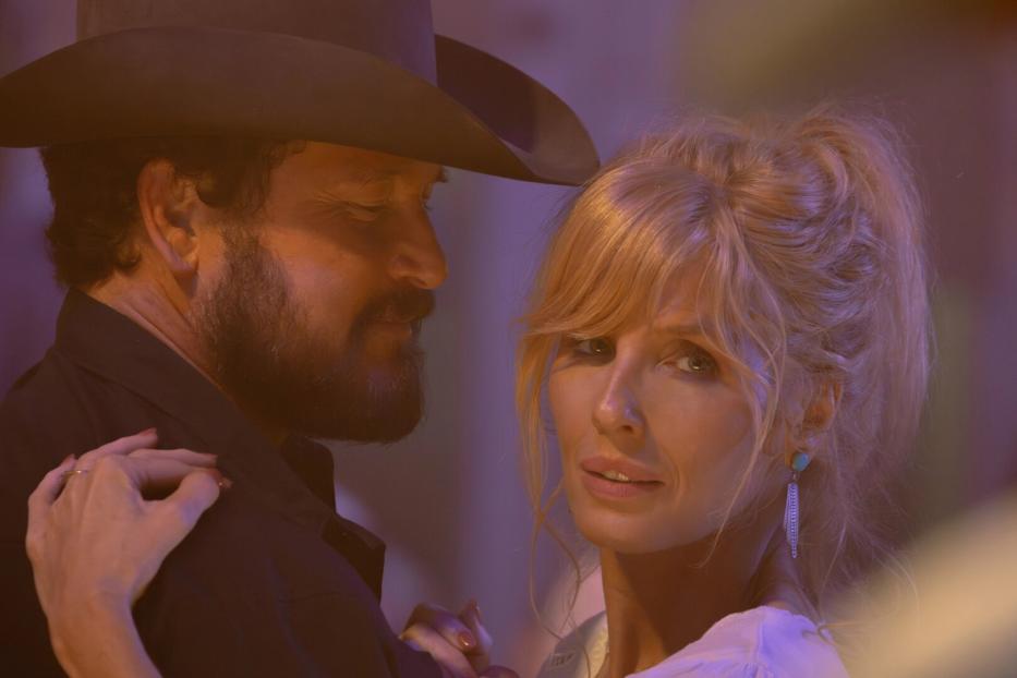 Ein Mann mit Bart und Cowboyhut tanzt eng mit einer blondhaarigen Frau, die nachdenklich in die Ferne blickt.