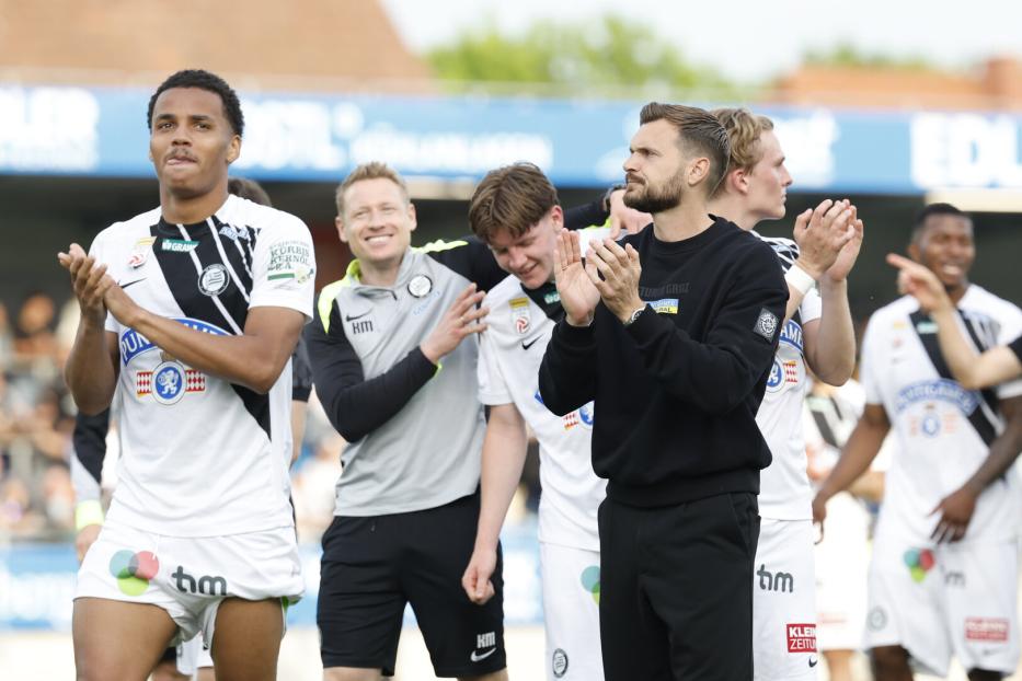 Eine Gruppe von SK Sturm Graz Spielern und Trainern applaudiert auf dem Rasen.