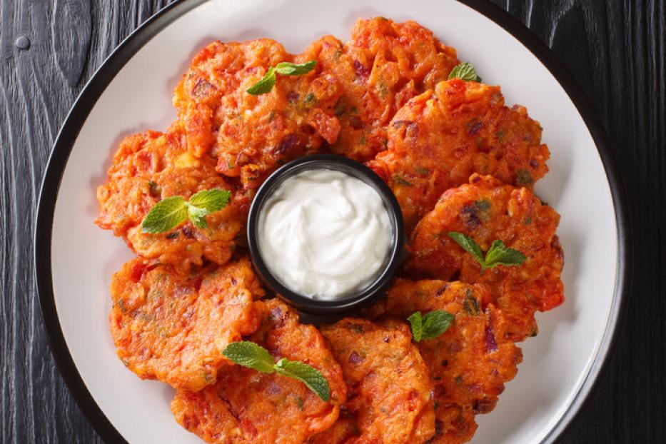 Tomatokeftedes, knusprige griechische Tomatenlaibchen, angerichtet mit Joghurtdip auf einem Teller.