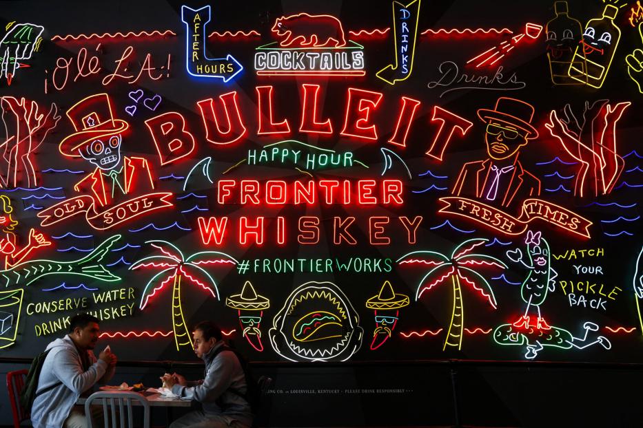 People eat in front of a sign for Bulleit Frontier Whiskey in Grand Central Market in Los Angeles