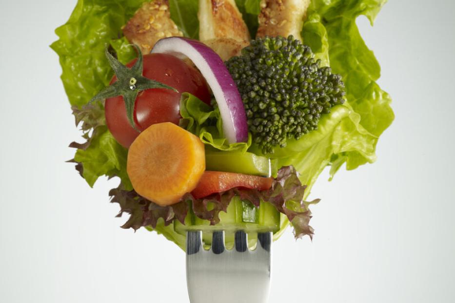Verschiedene Gemüsestücke, Salat und Hähnchenstreifen sind auf einer Gabel aufgespießt.