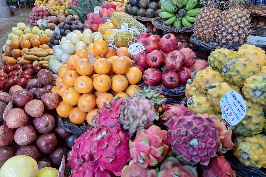 Auf einem Marktstand türmen sich exotische Früchte wie Drachenfrucht, Ananas, Bananen und Orangen.